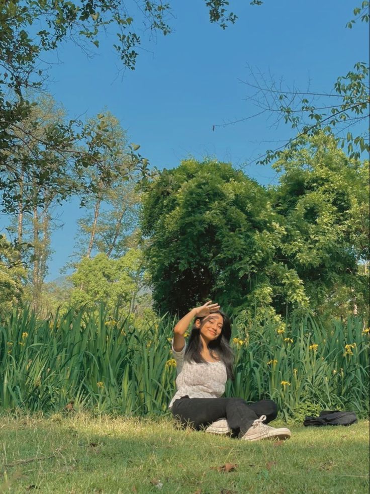 a woman sitting in the grass with her eyes closed and looking up into the sky