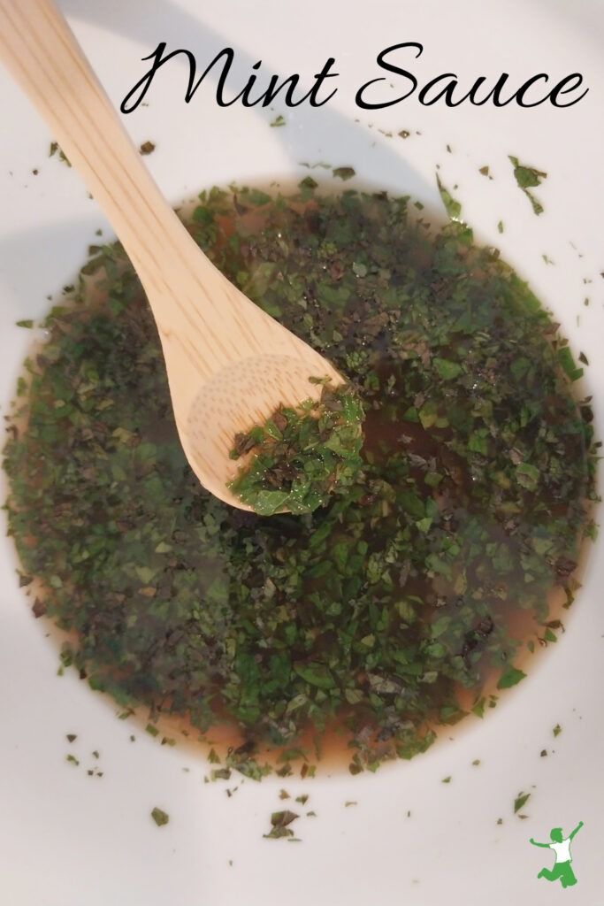 a wooden spoon in a white bowl filled with green herbs and mint sauce that says mint sauce