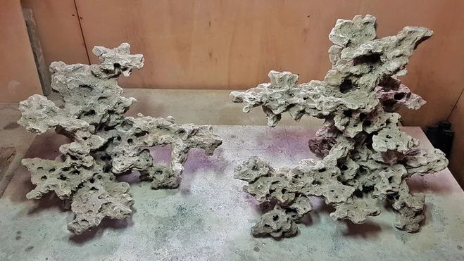 two sculptures made out of cement sitting on top of a wooden table next to a wall