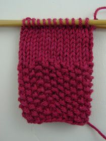 a pink knitted object hanging on a wooden stick with yarn in the foreground