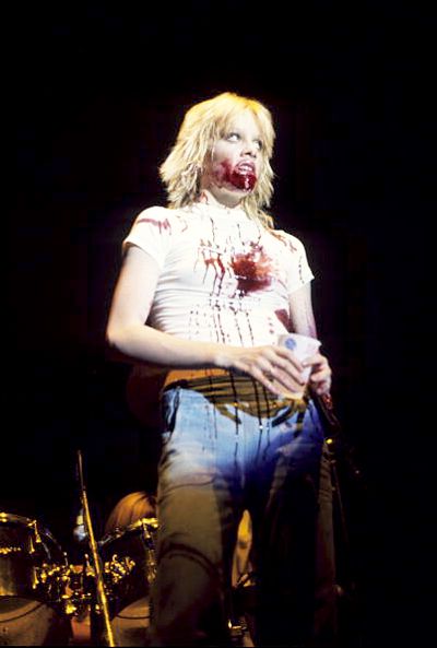 a woman with blood on her face standing in front of drums