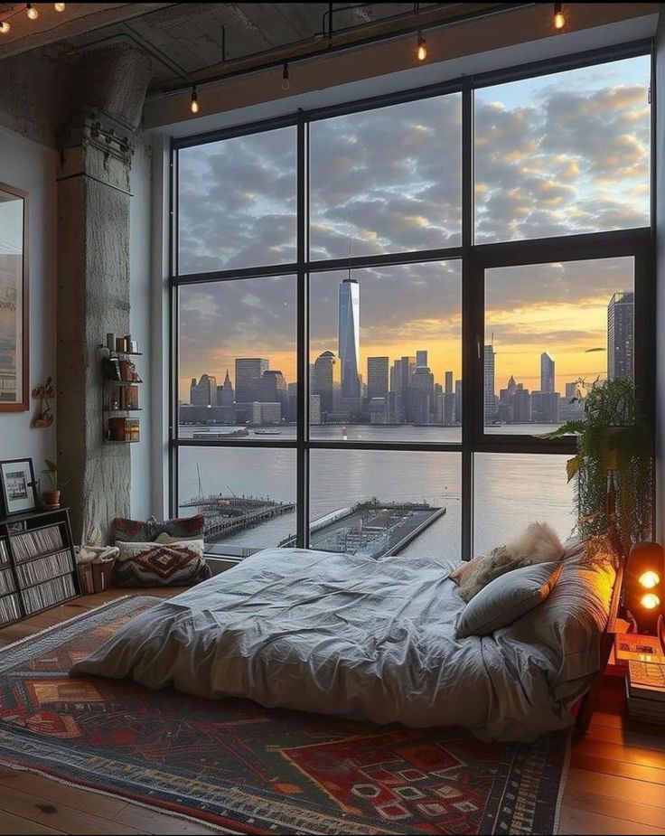 a bedroom with a large window overlooking the city at sunset or sunrise, and a bed in front of it