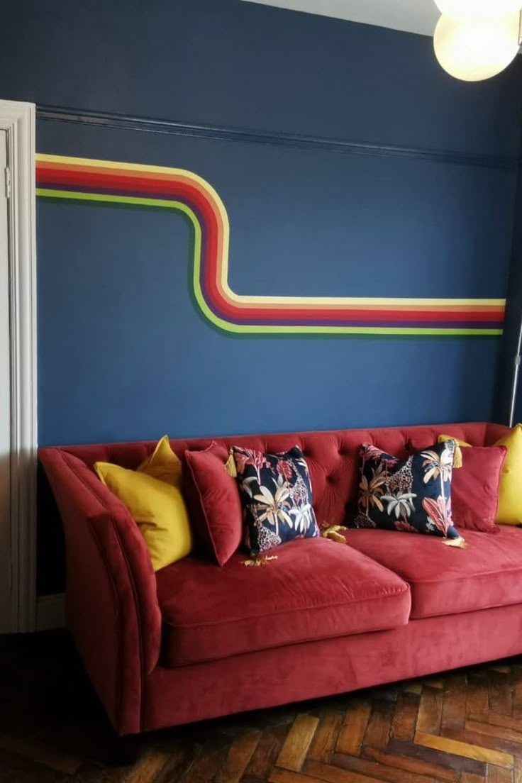 a red couch sitting in front of a blue wall with colorful pillows on it's back