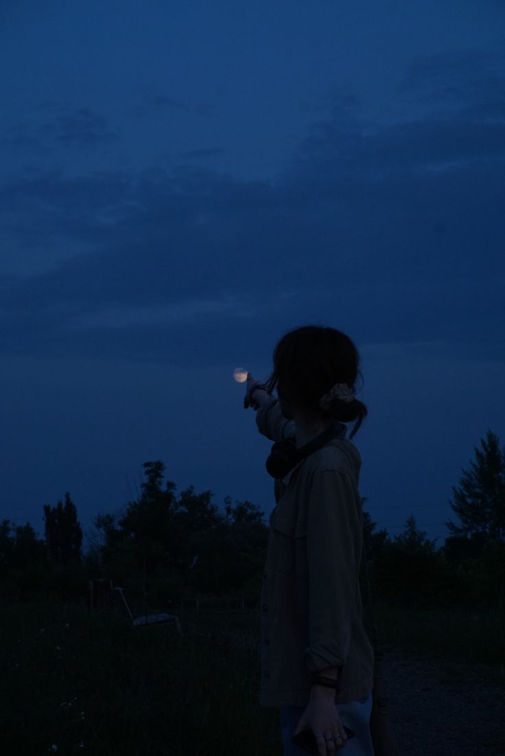 a person standing in the dark with a cell phone up to their ear and looking at something