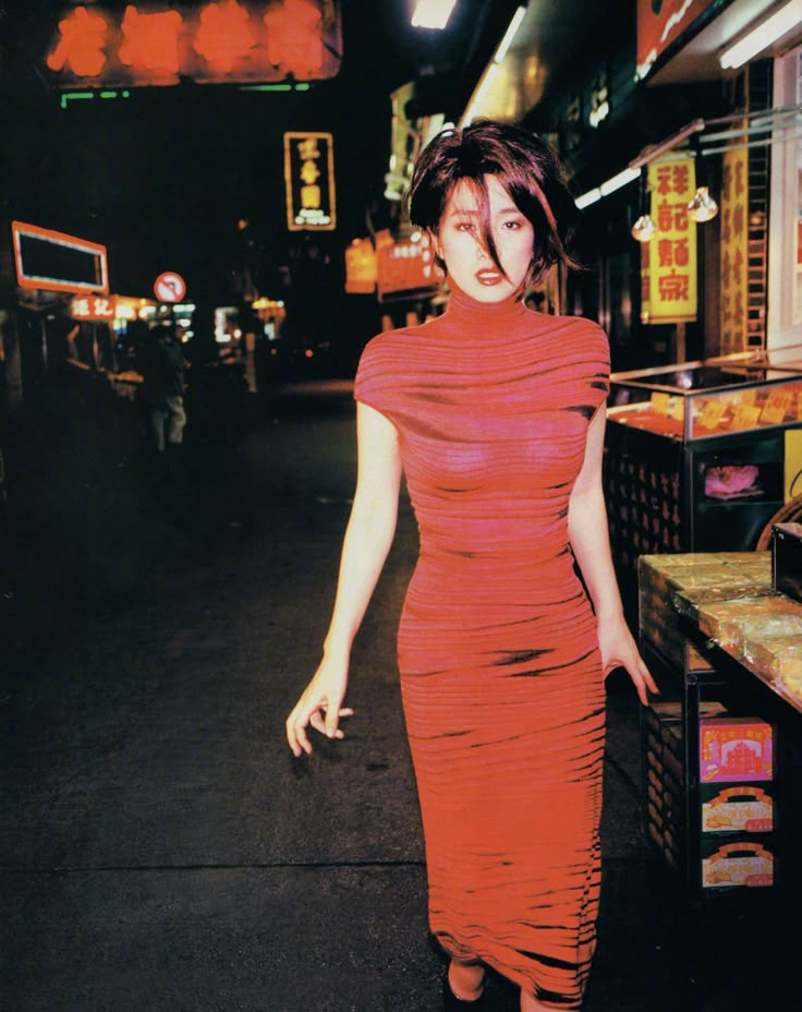 a woman in a red dress is walking down the street with her hand on her hip