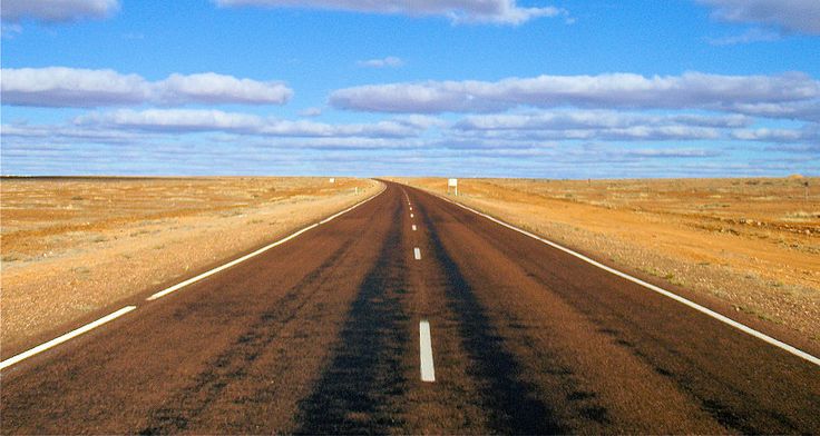 an empty road in the middle of nowhere on a clear day with blue skies and fluffy white clouds