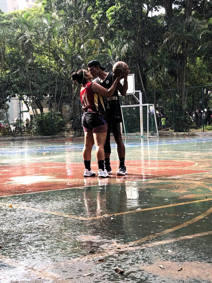 two people standing on a basketball court in the rain with their arms around each other