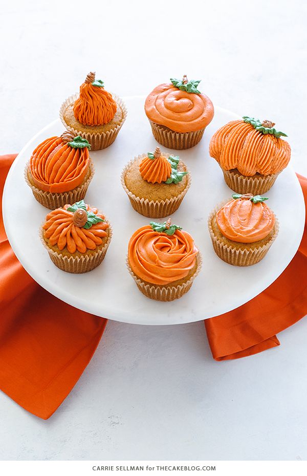 cupcakes with orange frosting are arranged on a white platter and an orange ribbon