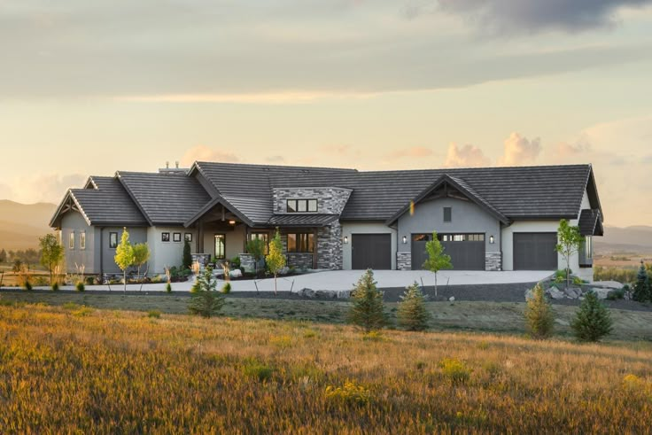 a large house in the middle of a field with mountains in the backgroud