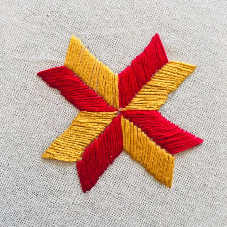 a red and yellow star is on a white cloth with some thread in the middle