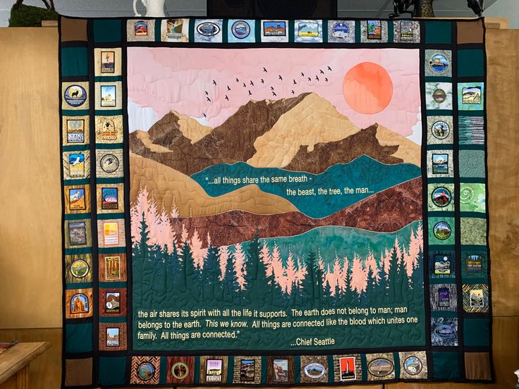 a quilted wall hanging with mountains and trees on it