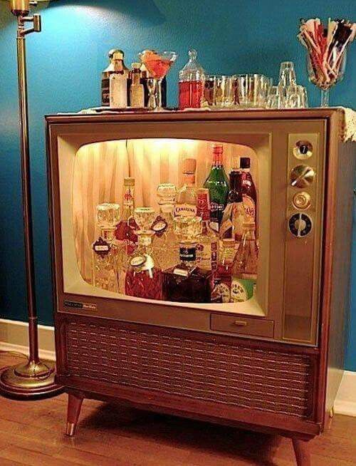 an old fashioned television with liquor bottles on it's side and a lamp next to it