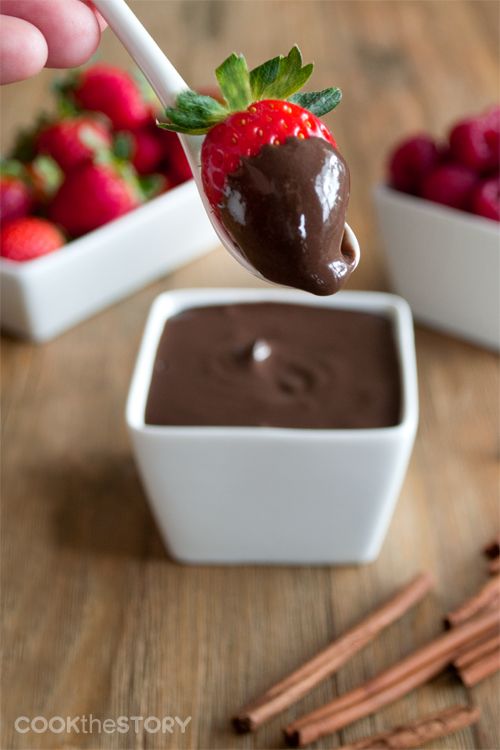 a spoon full of chocolate pudding with strawberries in the background