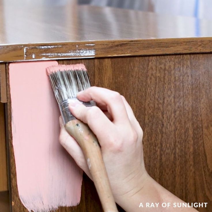 a person holding a paint brush in front of a wooden cabinet with pink paint on it