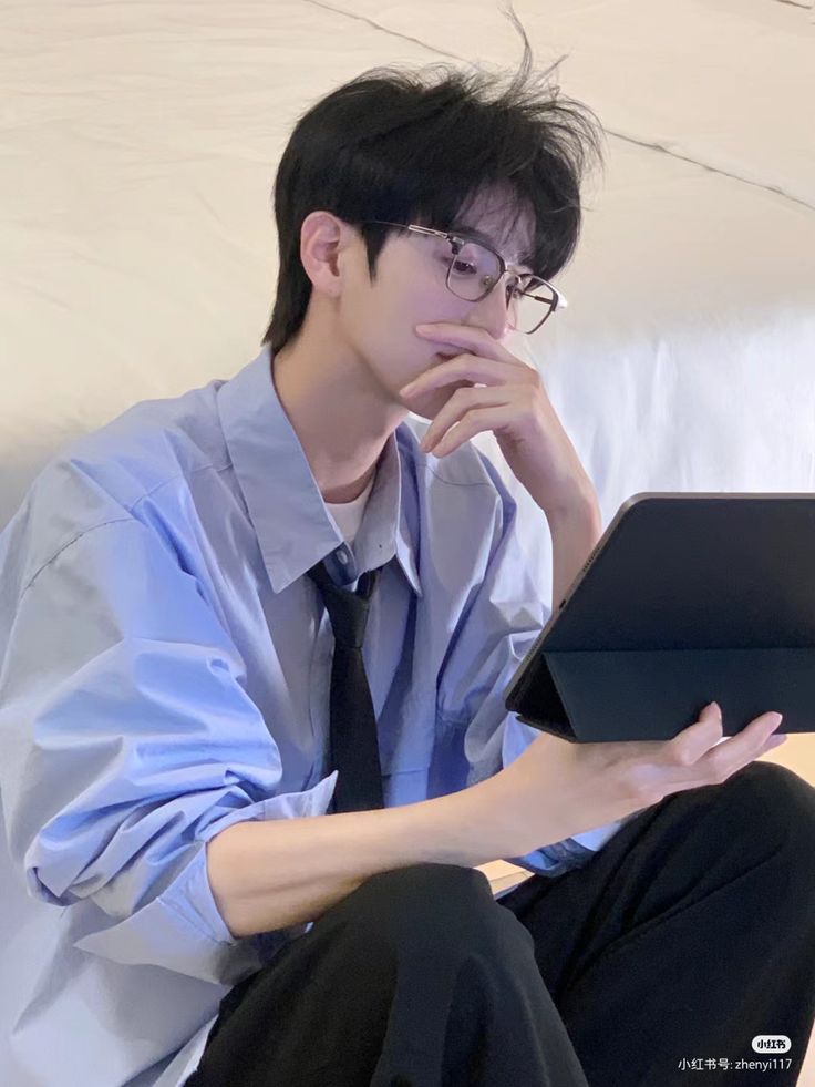 a young man sitting on a couch using a laptop computer while wearing glasses and a tie