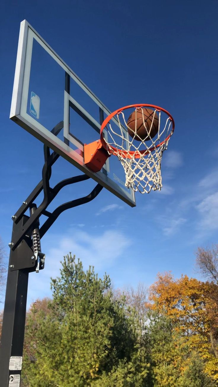 a basketball going through the hoop on a clear day with trees in the foreground