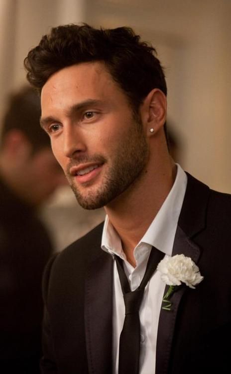 a man wearing a black suit and white flower in his lapel is looking at the camera