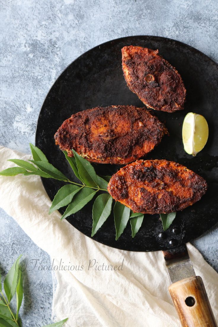 three pieces of meat sitting on top of a black plate next to a knife and some leaves