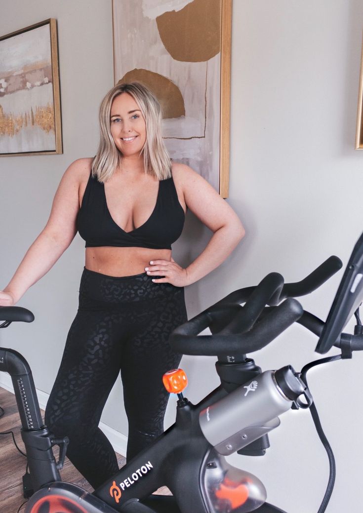 a woman standing next to an exercise bike with her arms on the handlebars