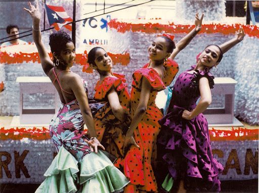 four women in colorful dresses are dancing on the street