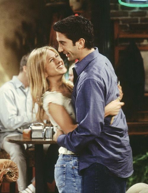 a man and woman hugging each other in front of a table with coffee cups on it