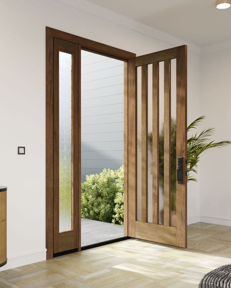 an open wooden door in a white room with wood flooring and large plant on the side