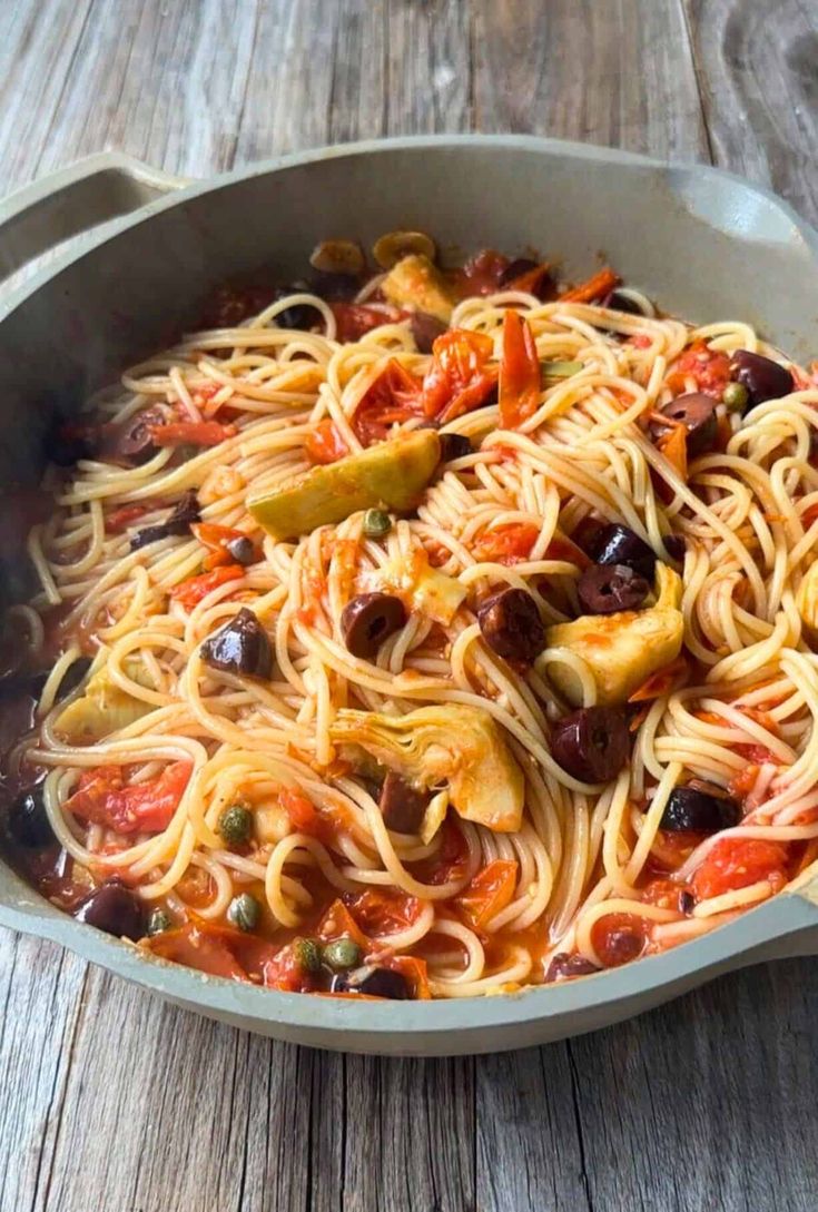 a pan filled with pasta and olives on top of a wooden table