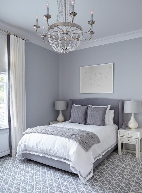 a white and gray bedroom with a chandelier hanging from the ceiling above the bed