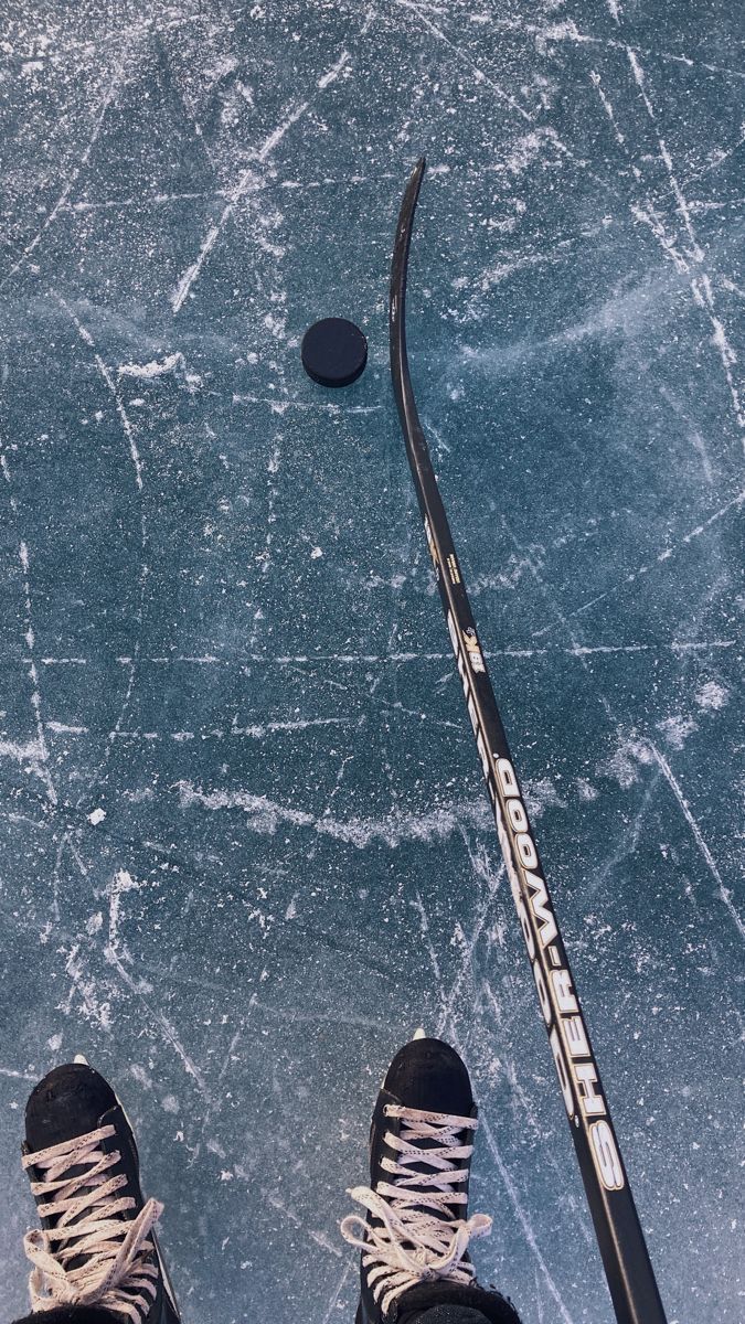 a person standing on an ice rink with their feet propped up next to a hockey stick