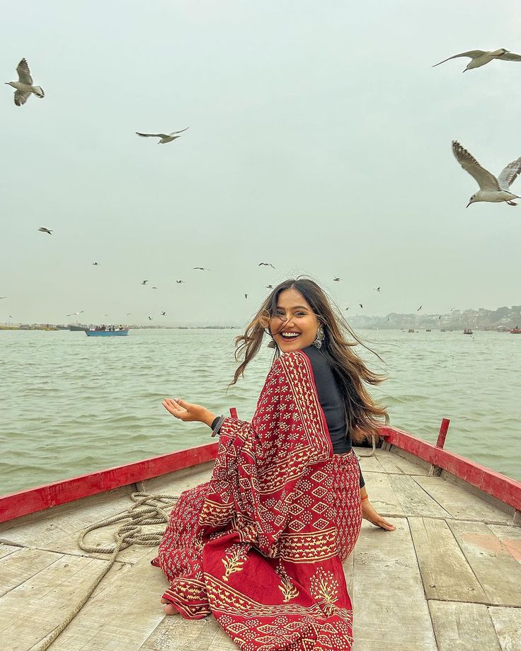 a woman sitting on the back of a boat with seagulls flying above her