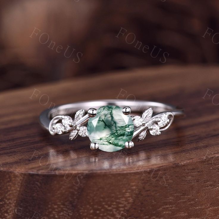 a ring with a green stone surrounded by leaves on top of a wooden table in front of a brown background