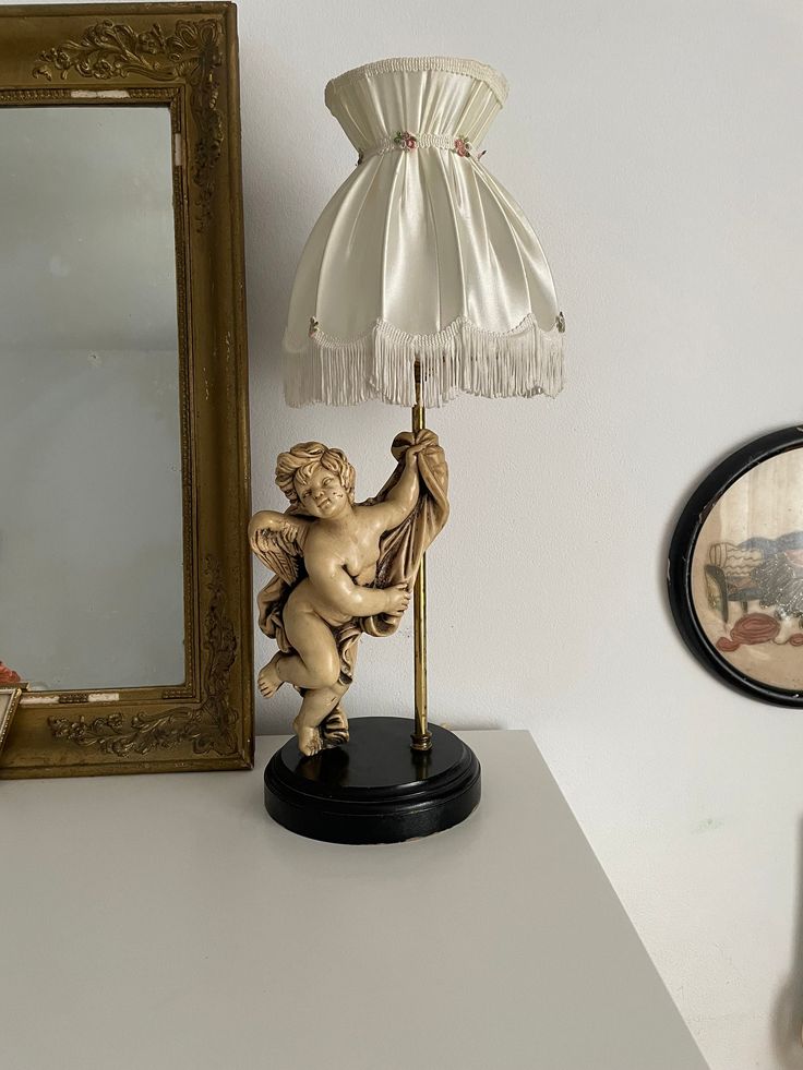 an angel figurine holding a lamp next to a mirror and framed photograph on the wall