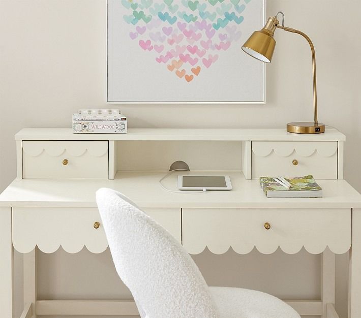 a white desk topped with a computer monitor next to a lamp and a painting on the wall