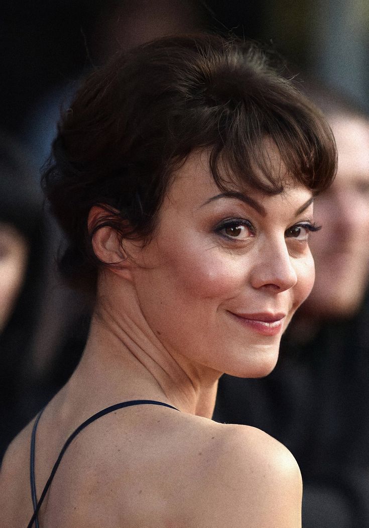 a close up of a person wearing a black dress and smiling at the camera with other people in the background