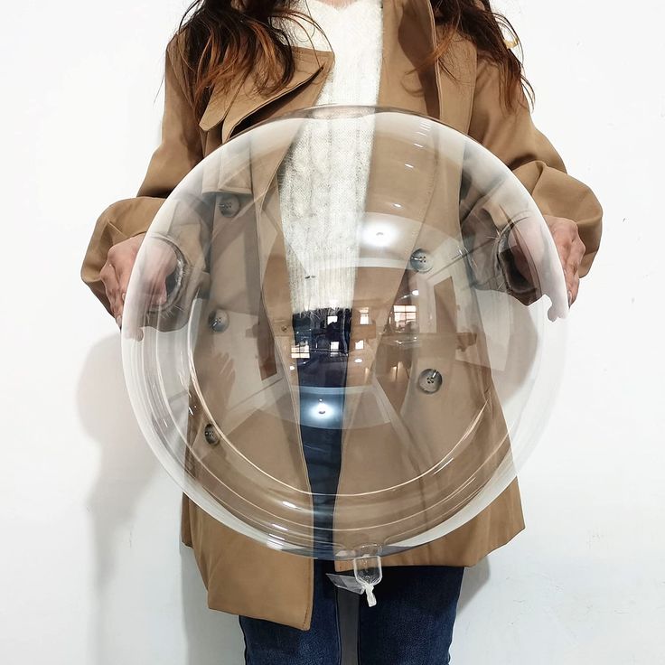 a woman holding a large clear object in front of her face and wearing a brown coat