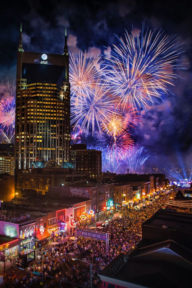 fireworks are lit up in the night sky over a city with tall buildings and lots of people