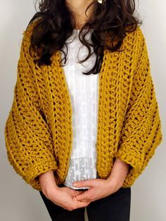 a woman standing in front of a white wall wearing a yellow knitted cardigan