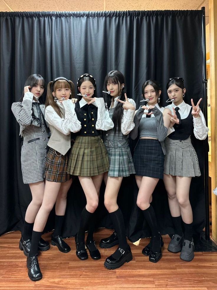 four girls in school uniforms posing for the camera with their hands up and one pointing