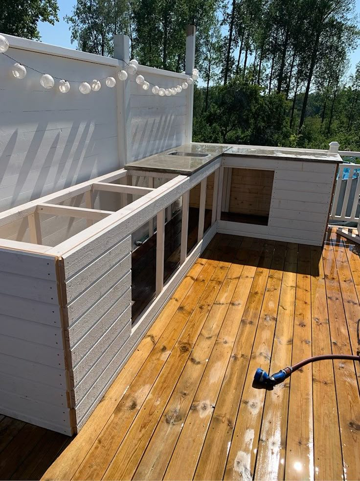 an outdoor kitchen on a deck with wood flooring and white walls, built into the side of a house