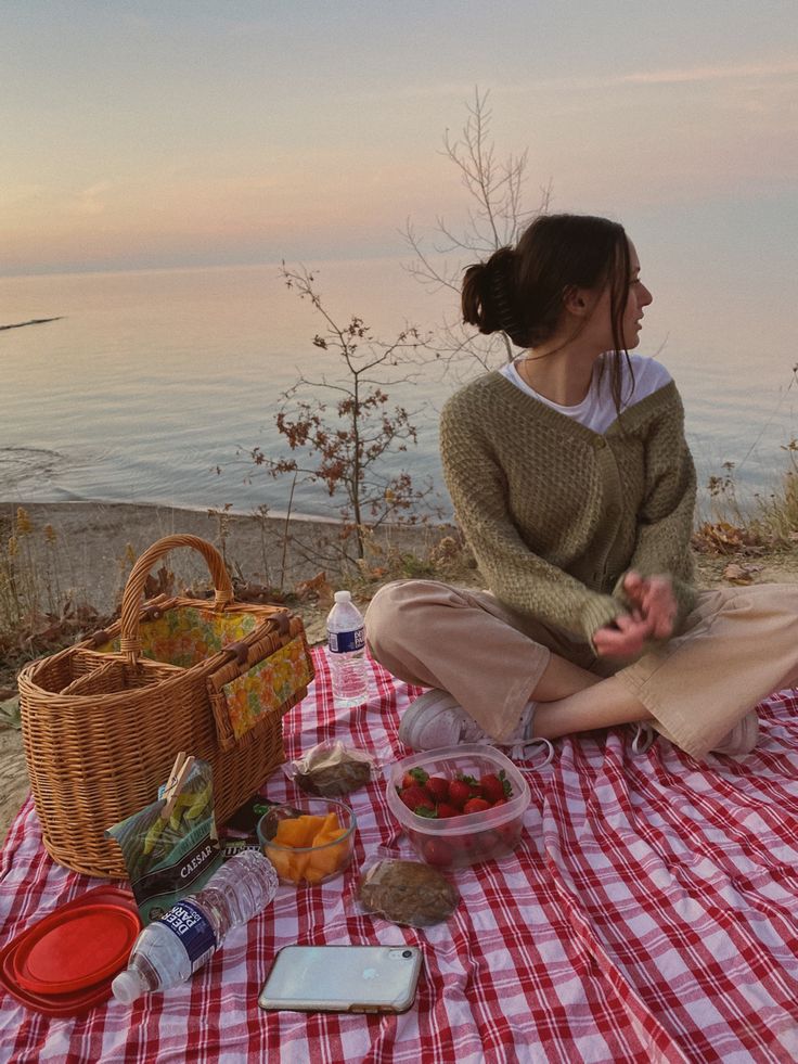 a woman sitting on top of a red and white checkered blanket next to a basket