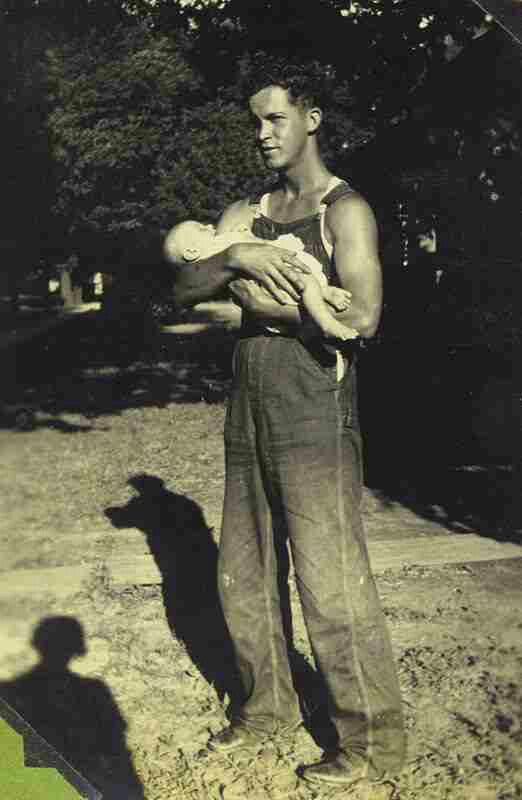 an old black and white photo of a man holding a baby in his arms while standing outside