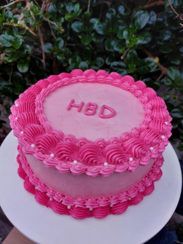 a pink cake sitting on top of a white plate next to green plants and bushes