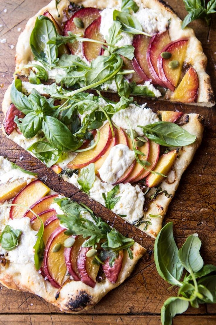 a pizza topped with sliced peaches, spinach and feta cheese on a wooden cutting board