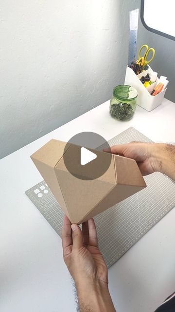 a person is holding an open box on top of a white table next to a window