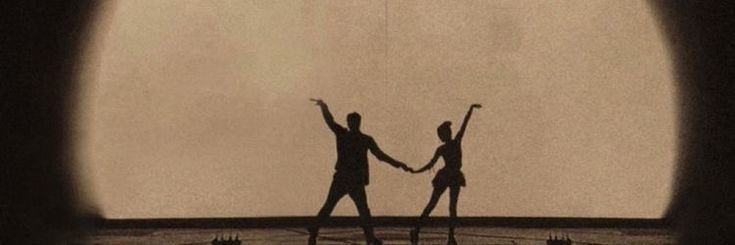 two people holding hands while standing in front of a clock with their arms raised up