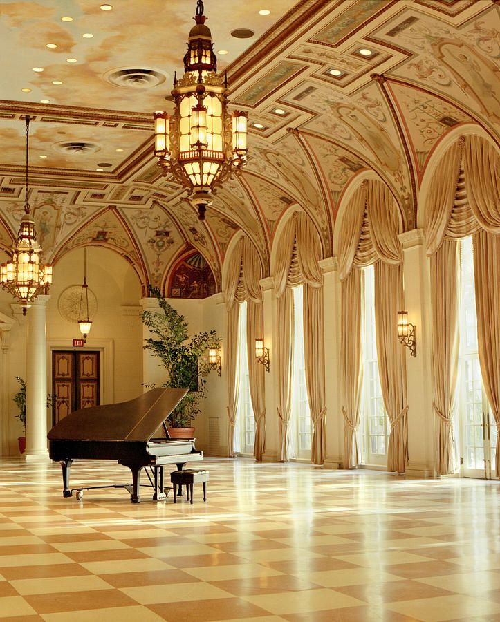 a grand piano in the middle of a large room with chandeliers and windows