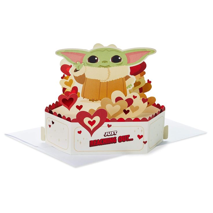 an origami baby yoda in a box with hearts on the bottom and eyes