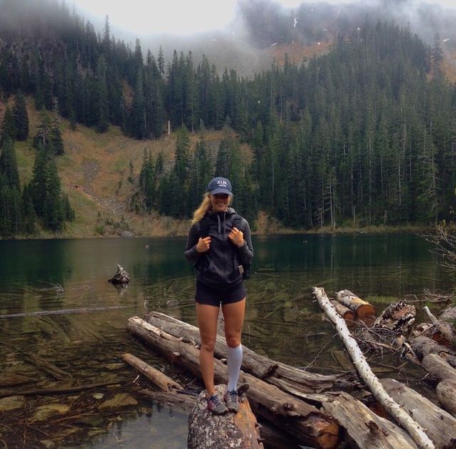 a woman standing on top of a log in the middle of a forest next to a lake