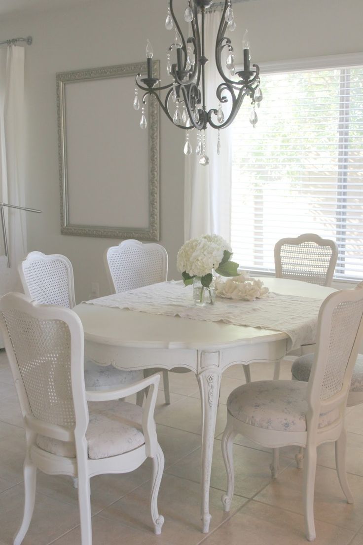 a chandelier hangs from the ceiling above a white dining room table and chairs