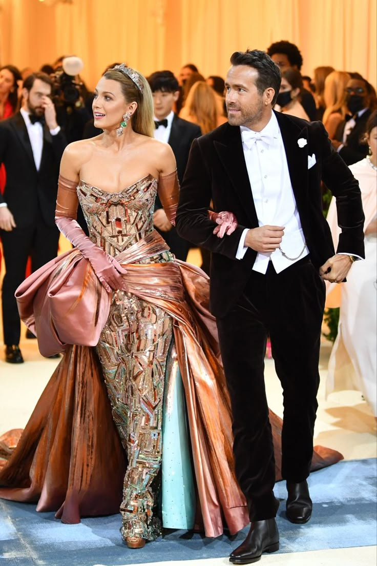 a man in a tuxedo walking next to a woman in a gown on a blue carpet